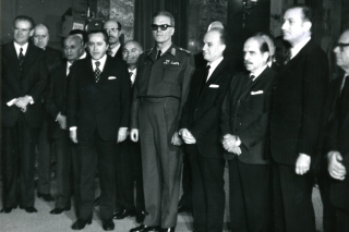 Το πρώτο κλιμάκιο του υπουργικού συμβουλίου της χούντας Ιωαννίδη (26/11/1973). Στη μέση, ένστολος ο «Πρόεδρος της Δημοκρατίας» Φίδων Γκιζίκης, στα αριστερά του ο «πρωθυπουργός» Αδαμάντιος Ανδρουτσόπουλος